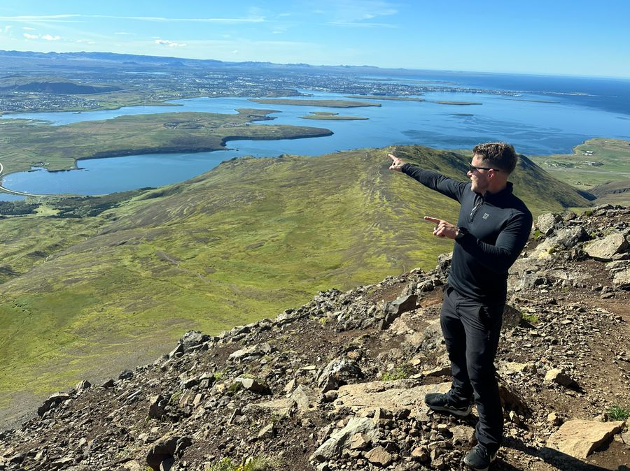 Siggi on a rocky mountain ridge pointing out over Reykjavík and the bay