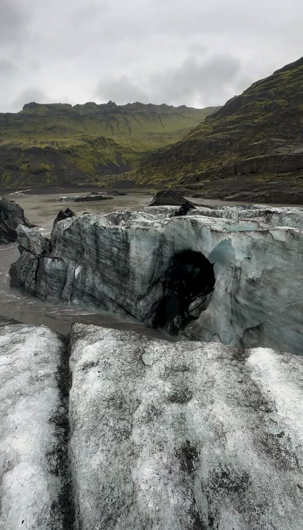 Grey glacier ice and an ice cave below green mountains